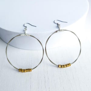 May include: A pair of silver hoop earrings with gold beads. The earrings are made from guitar strings.