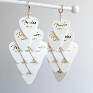 May include: White dangle earrings made from multiple layers of white guitar picks with gold lettering that reads "Fender Heavy".