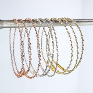May include: Five guitar strings in different colors, including gold, silver, and copper, are displayed on a metal stand. The strings are wound and have a decorative pattern.