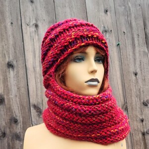 May include: A red knitted hat and cowl set. The hat and cowl are made of a chunky yarn with flecks of yellow, purple, and orange. The set is displayed on a mannequin head against a wooden background.