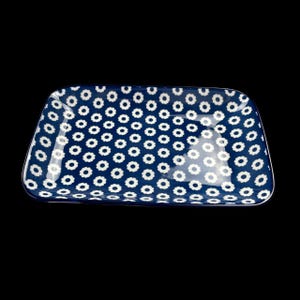 May include: A rectangular ceramic serving dish with a dark blue background and a repeating pattern of small white flower shapes. The dish has rounded corners and a glossy finish, suitable for serving food.