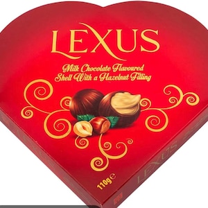 May include: A heart-shaped red box of Lexus milk chocolate flavored shell with a hazelnut filling. The box features gold text and swirling gold decorative patterns, with an illustration of chocolates and hazelnuts. The net weight is 110g.