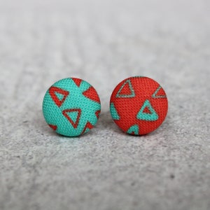 May include: A pair of fabric earrings with a geometric pattern. One earring is turquoise with red triangles and the other is red with turquoise triangles.