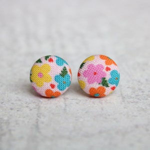 May include: A pair of small, round, pink fabric earrings with a floral pattern in yellow, blue, orange, and green.