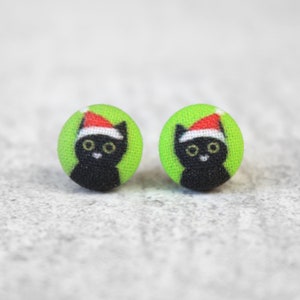 May include: A pair of green fabric earrings with a black cat wearing a red Santa hat design.