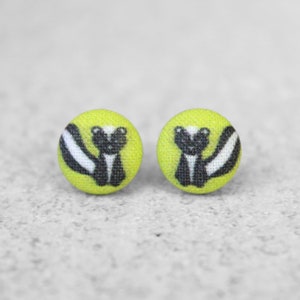 May include: A pair of yellow button earrings with a black and white skunk design.