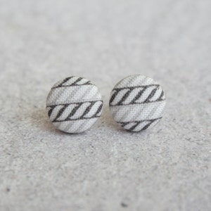 May include: A pair of small, round stud earrings with a white and black striped fabric design.