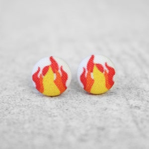 May include: A pair of white button earrings with a red and yellow flame design.