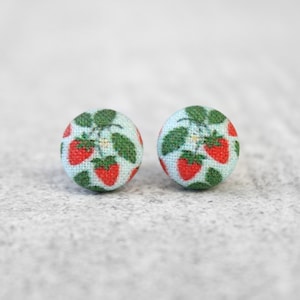 May include: A pair of small, round stud earrings with a light blue background and a pattern of red strawberries.