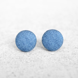 May include: A pair of denim fabric stud earrings. The earrings are a light blue color and have a circular shape.