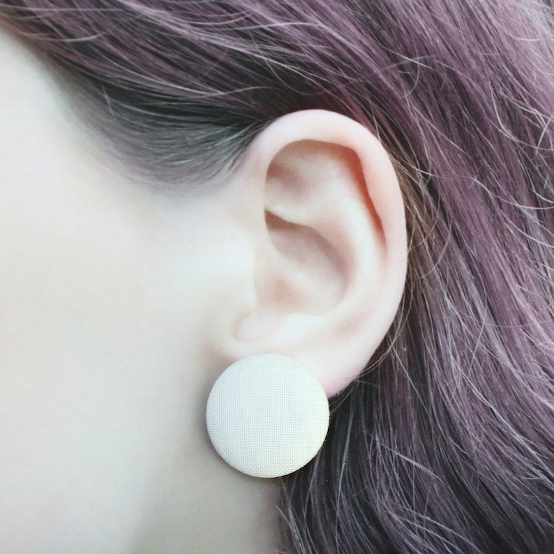 May include: A close-up of a person's ear with a white fabric button earring.