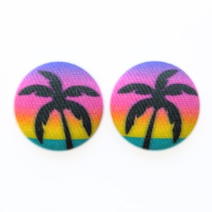 May include: A pair of colorful oval-shaped earrings with a silhouette of a palm tree against a sunset gradient background.