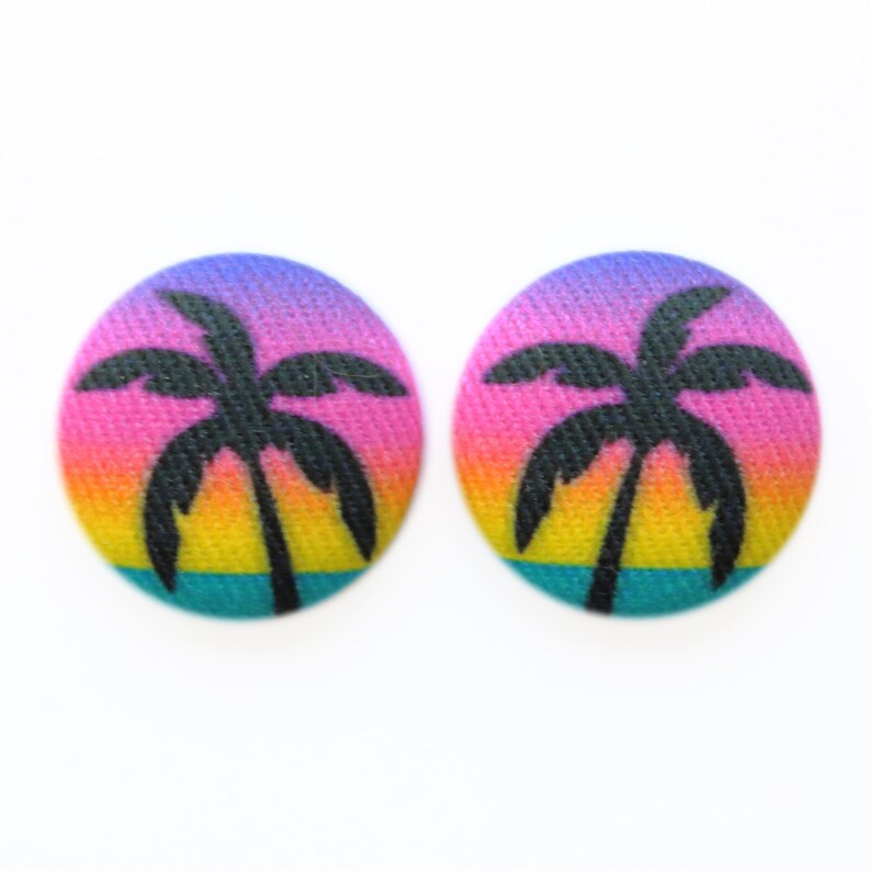 May include: A pair of colorful oval-shaped earrings with a silhouette of a palm tree against a sunset gradient background.