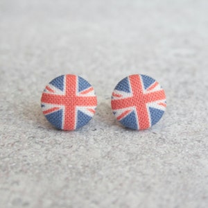 May include: A pair of stud earrings featuring a red, white, and blue Union Jack design. The earrings are made of fabric and have a circular shape.