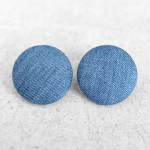 May include: A pair of blue denim fabric earrings. The earrings are round and have a smooth texture.