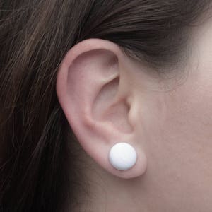 May include: A close-up of a person's ear with a white button-shaped earring.