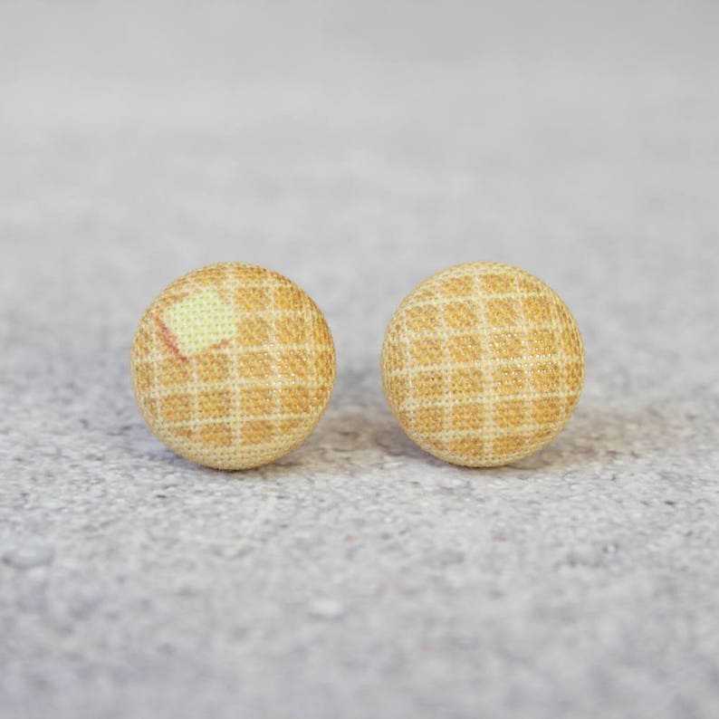 May include: A pair of small, round, yellow and white fabric earrings with a checkered pattern.