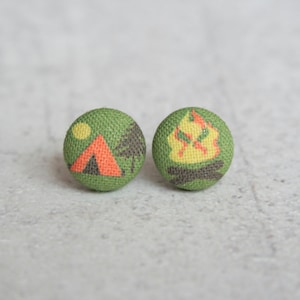 May include: A pair of green fabric button earrings with a camping theme. One earring features a tent, a tree, and a sun. The other earring features a campfire with flames.