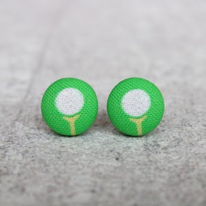May include: A pair of green fabric stud earrings with a white golf ball and yellow tee design.