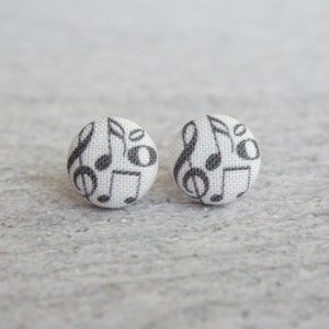 May include: A pair of white fabric stud earrings with a black musical note pattern.