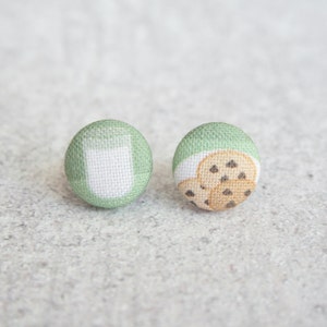 May include: A pair of green fabric button earrings. One earring features a white milk carton design, and the other earring features a design of three chocolate chip cookies.