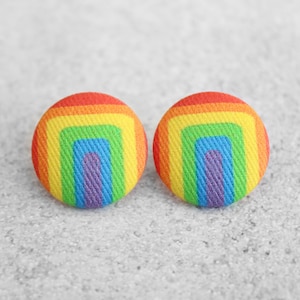 May include: A pair of rainbow-colored fabric button earrings. The buttons are round and have a concentric circle design with a purple center.