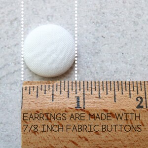 May include: A white fabric button measuring 7/8 inch in diameter. The button is next to a ruler with the text "EARRINGS ARE MADE WITH 7/8 INCH FABRIC BUTTONS".