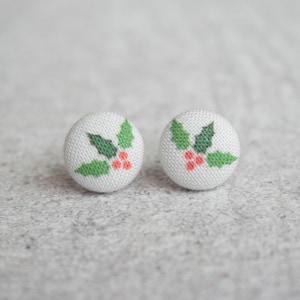 May include: A pair of white fabric earrings with a green holly leaf and red berry design.