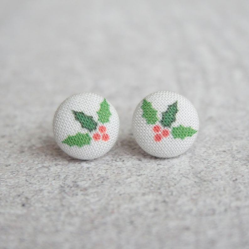 May include: A pair of white fabric earrings with a green holly leaf and red berry design.