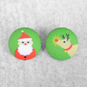 May include: A pair of green button earrings with a Christmas theme. One earring features a Santa Claus design, while the other features a reindeer design.