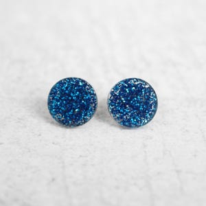 May include: A pair of blue glitter stud earrings. The earrings are round and have a silver backing.