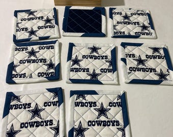 May include: A collection of eight square quilted coasters in navy blue and white. Each coaster displays the text "COWBOYS" and a star emblem. A small wooden box is also visible in the image.