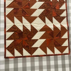 Puede incluir: Una colcha marrón y blanca con un patrón geométrico. La colcha está hecha de cuadrados y triángulos, y el patrón se repite en toda la colcha.