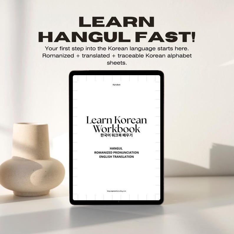May include: A digital tablet displaying a workbook cover with the title "Learn Korean Workbook" in black text. The subtitle is "한국어 워크북 배우기" in Korean. The cover also includes the words "HANGUL, ROMANIZED PRONUNCIATION, ENGLISH TRANSLATION" in black text.