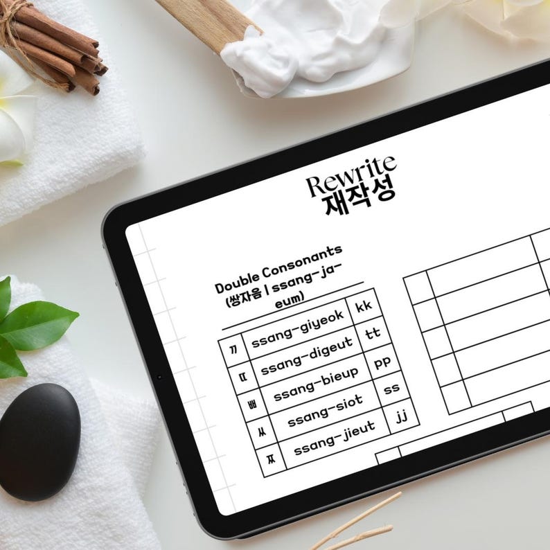 May include: A black and white worksheet on a tablet with the title "Rewrite 재작성" and the heading "Double Consonants (쌍자음 | ssang-ja-eum)". The worksheet lists Korean consonants and their corresponding double consonant forms.