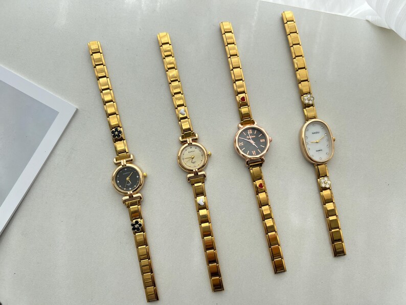 Op de afbeelding: Vijf gouden polshorloges met verschillende wijzerplaatontwerpen. De horloges hebben gouden metalen banden met decoratieve accenten.