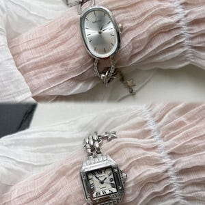 K&ouml;nnte beinhalten: Zwei silberne Uhren mit Gliederarmb&auml;ndern. Die obere Uhr hat ein ovales Zifferblatt mit dem Wort "NAIDU" darauf. Die untere Uhr hat ein quadratisches Zifferblatt mit r&ouml;mischen Ziffern und dem Wort "QUARTZ" darauf.