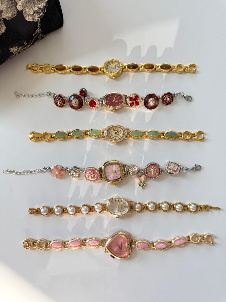 May include: Six decorative women's watches with various designs. The watches have gold-toned metal bands and feature different face shapes, including round, oval, and heart-shaped. Some watches have gemstone or pearl accents, and others have floral or decorative elements.
