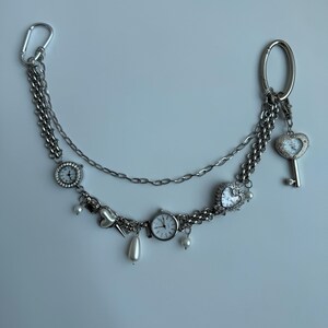 Puede incluir: Accesorio de cadena plateada con m&uacute;ltiples esferas de reloj peque&ntilde;as, dijes en forma de coraz&oacute;n y un colgante de llave. La cadena est&aacute; adornada con perlas de imitaci&oacute;n y un mosquet&oacute;n. Una pieza decorativa &uacute;nica.