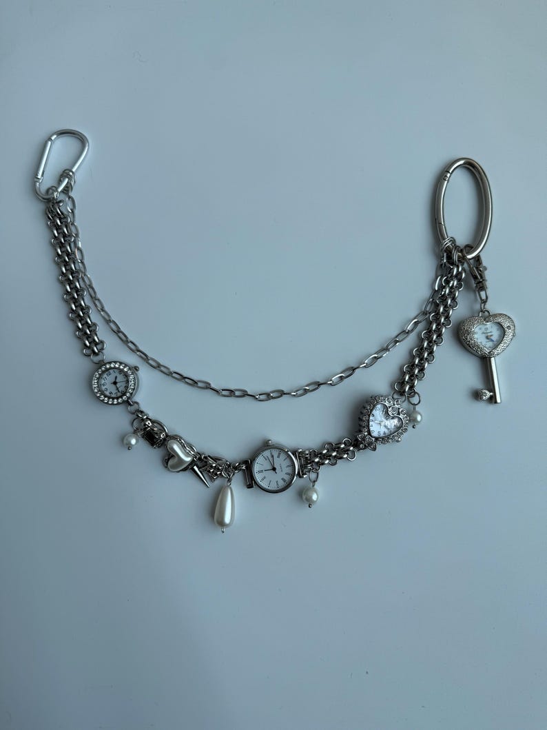Puede incluir: Accesorio de cadena plateada con m&uacute;ltiples esferas de reloj peque&ntilde;as, dijes en forma de coraz&oacute;n y un colgante de llave. La cadena est&aacute; adornada con perlas de imitaci&oacute;n y un mosquet&oacute;n. Una pieza decorativa &uacute;nica.