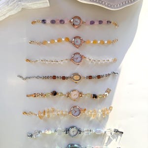 Pu&ograve; includere: Una collezione di sette orologi da polso con perline con varie pietre preziose e perle colorate. I quadranti degli orologi sono rotondi con numeri romani. I cinturini sono in metallo dorato e argentato. Le pietre preziose includono cristalli rosa, gialli e trasparenti.