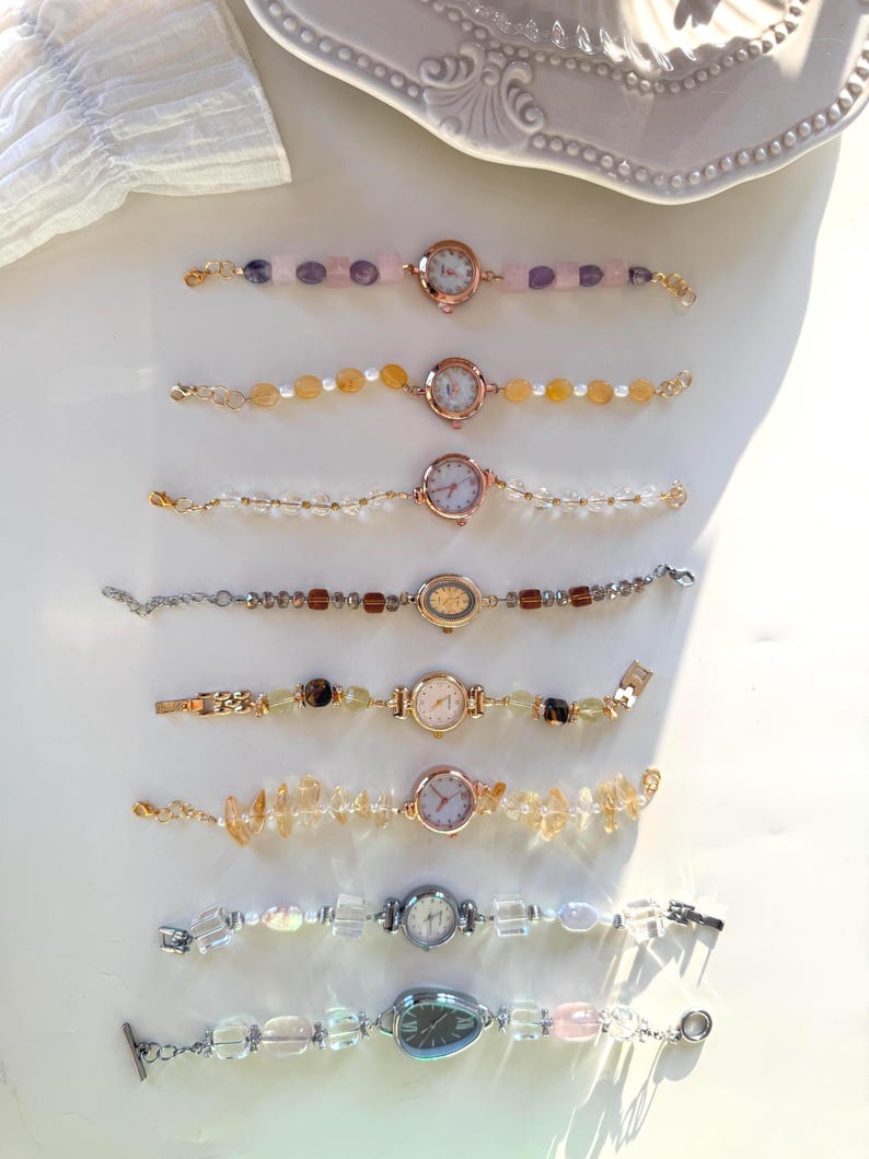 Pu&ograve; includere: Una collezione di sette orologi da polso con perline con varie pietre preziose e perle colorate. I quadranti degli orologi sono rotondi con numeri romani. I cinturini sono in metallo dorato e argentato. Le pietre preziose includono cristalli rosa, gialli e trasparenti.