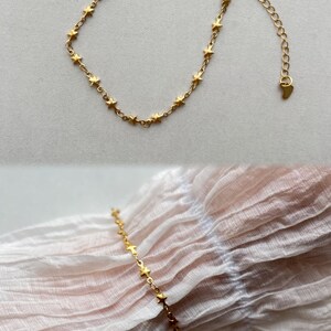Puede incluir: Un brazalete de cadena dorada en forma de estrella con un cierre en forma de coraz&oacute;n. El brazalete se muestra sobre un fondo de tela blanca.