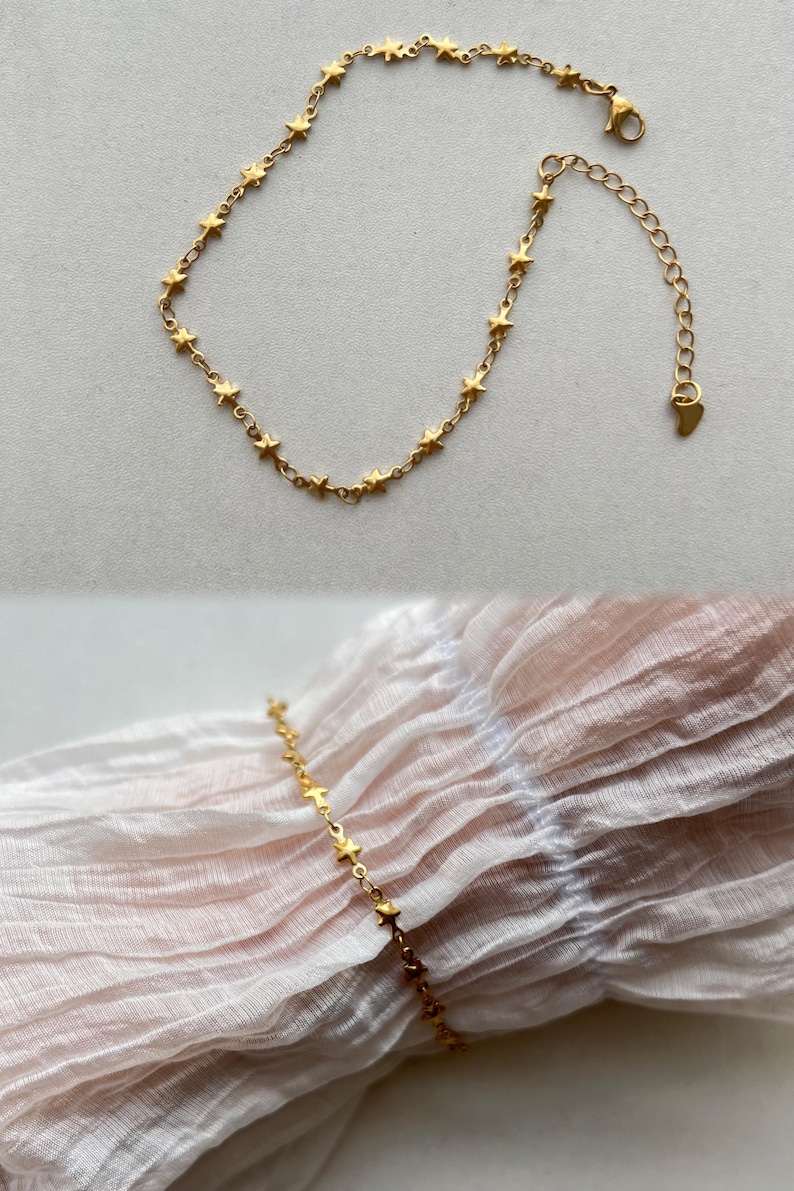 Puede incluir: Un brazalete de cadena dorada en forma de estrella con un cierre en forma de coraz&oacute;n. El brazalete se muestra sobre un fondo de tela blanca.