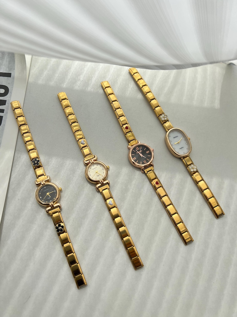 Op de afbeelding: Vijf gouden polshorloges met verschillende wijzerplaatontwerpen. Elk horloge heeft een gouden metalen band met kleine decoratieve accenten.