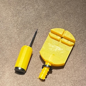 May include: A yellow and black air pump and a yellow plastic tool. The air pump has a yellow cylinder with a black base and a black needle. The plastic tool has a yellow body with a black ring and a yellow base.