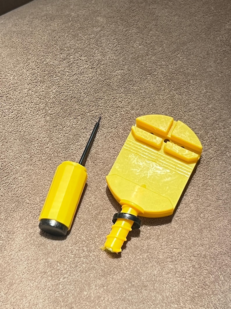 May include: A yellow and black air pump and a yellow plastic tool. The air pump has a yellow cylinder with a black base and a black needle. The plastic tool has a yellow body with a black ring and a yellow base.