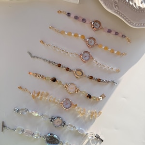 Pu&ograve; includere: Una collezione di delicati orologi da polso con perline e pietre preziose colorate e quadranti in metallo. I cinturini degli orologi presentano perline trasparenti, rosa, gialle e marroni. I quadranti degli orologi sono rotondi o ovali.