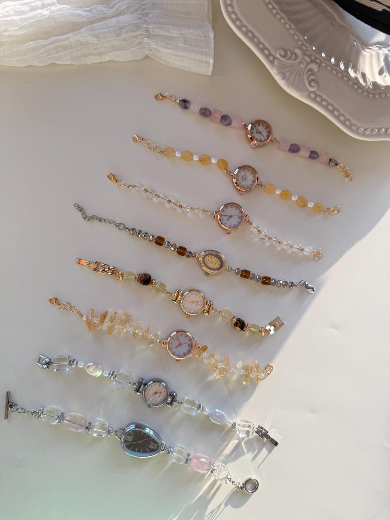 Pu&ograve; includere: Una collezione di delicati orologi da polso con perline e pietre preziose colorate e quadranti in metallo. I cinturini degli orologi presentano perline trasparenti, rosa, gialle e marroni. I quadranti degli orologi sono rotondi o ovali.