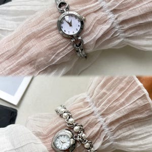 K&ouml;nnte beinhalten: Zwei silberne Armbanduhren mit wei&szlig;en Zifferbl&auml;ttern. Die erste Uhr hat ein Armband mit herzf&ouml;rmigen Gliedern. Die zweite Uhr hat ein herzf&ouml;rmiges Zifferblatt und ein Armband mit Perlenbesatz.
